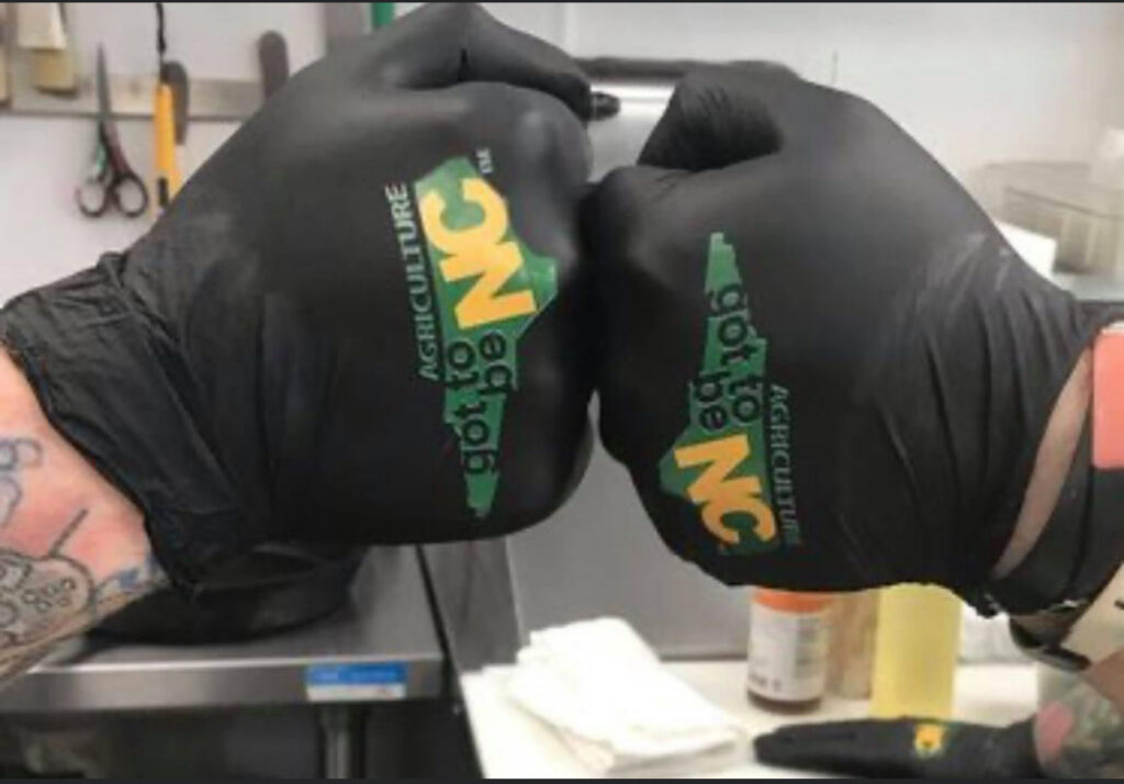 two gloved hands each with the GotToBeNc logo bumping fists